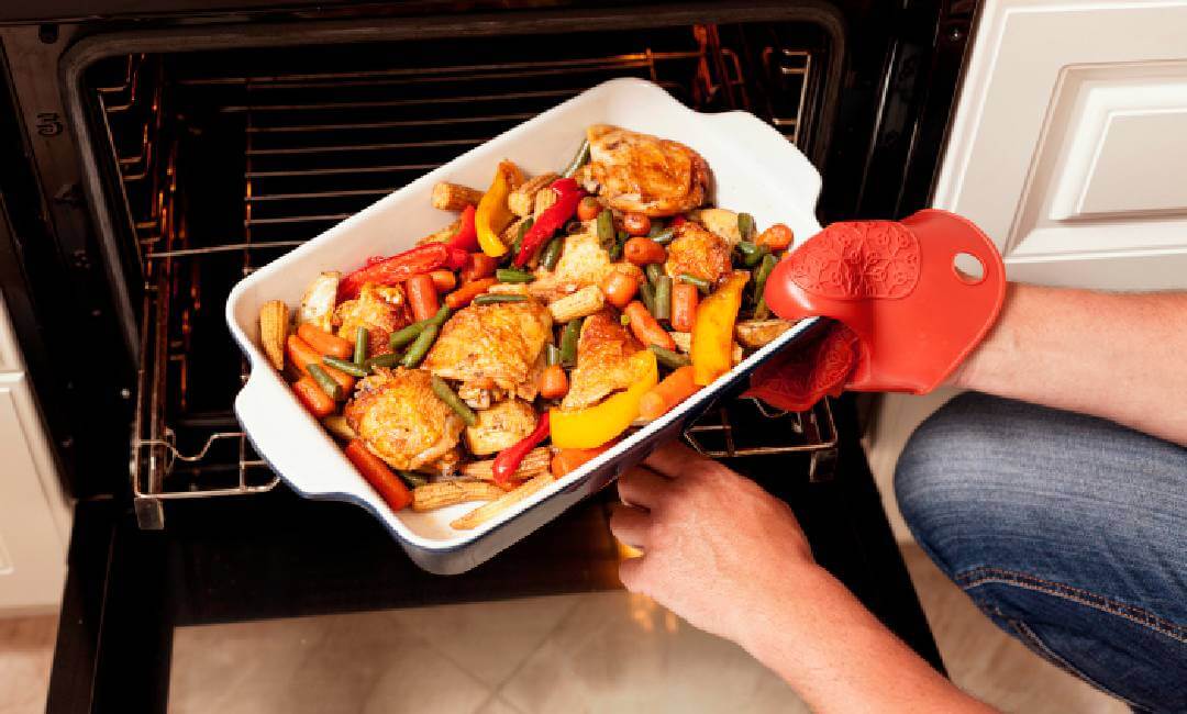 chicken and roasted vegetables baking in an oven tray being removed with oven mitt