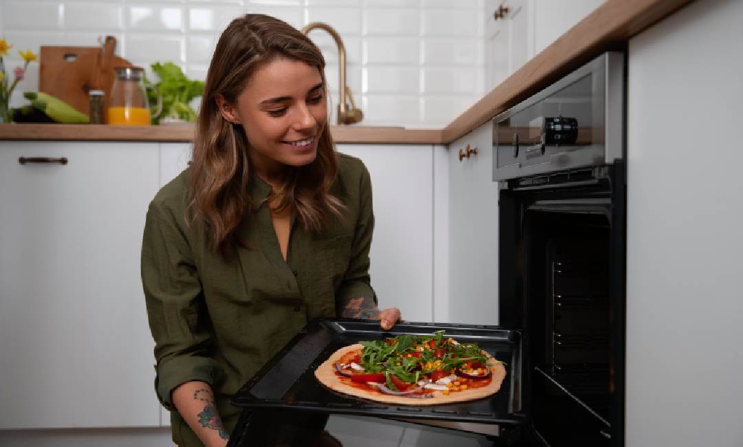 woman taking homemade pizza out of an air fryer oven in a modern kitchen