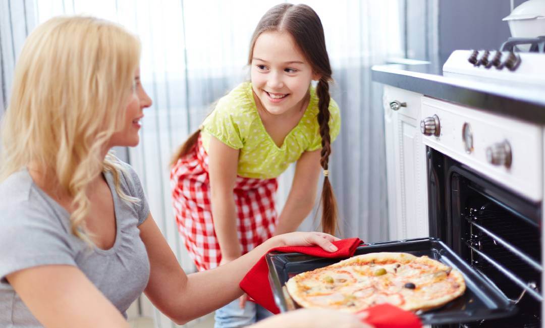 mother taking pizza out of an air fryer oven while child watches in kitchen