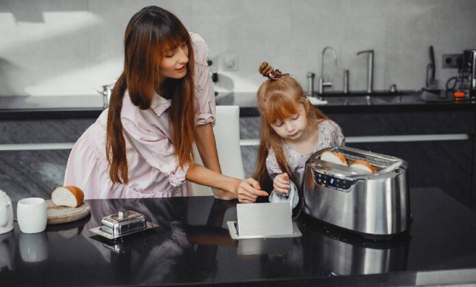 Mother helping daughter use a toaster while making breakfast in a modern kitchen
