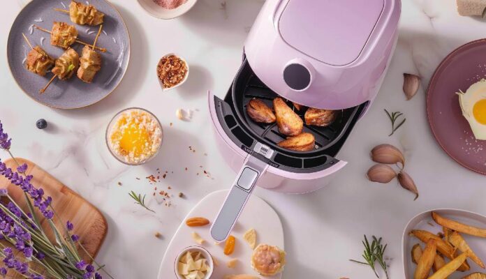 Pink air fryer cooking crispy chicken wings with spices and side dishes on kitchen table