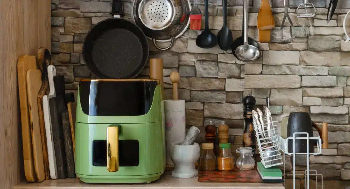 Green non-toxic air fryer on a kitchen counter with cookware and utensils nearby