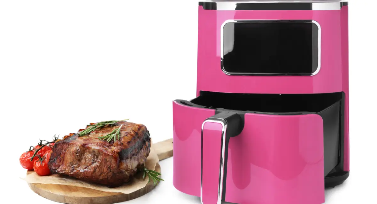 Cooked steak with herbs and tomatoes beside a pink air fryer with the basket pulled open