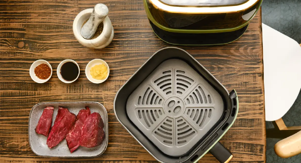 Air fryer basket beside sliced steak and seasonings on a wooden table before reheating