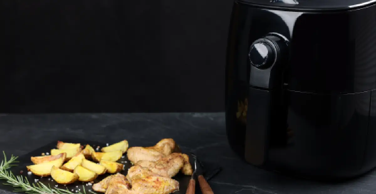 Small black air fryer beside cooked chicken wings and potato wedges during testing